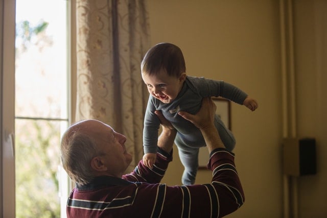 A grandfather holds a baby over his head like it's an airplane