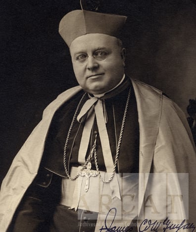 Black-and-white portrait of James Cardinal McGuigan in a seated pose wearing episcopal dress, biretta and ferraiolo.