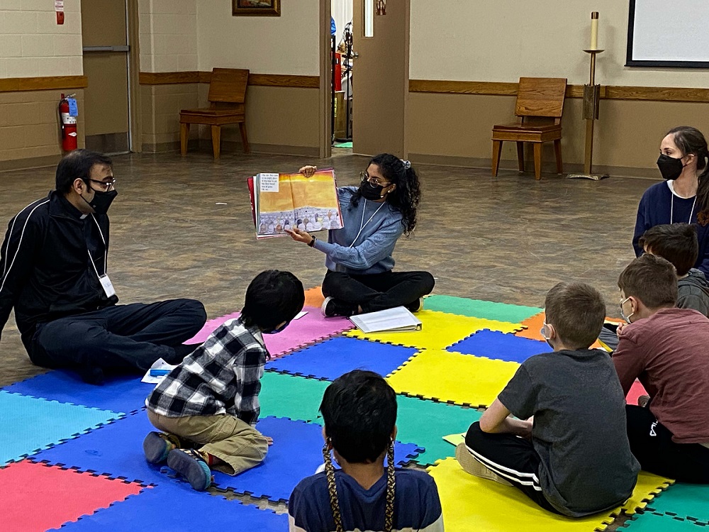 Adults and children sit on the floor as a book is read aloud