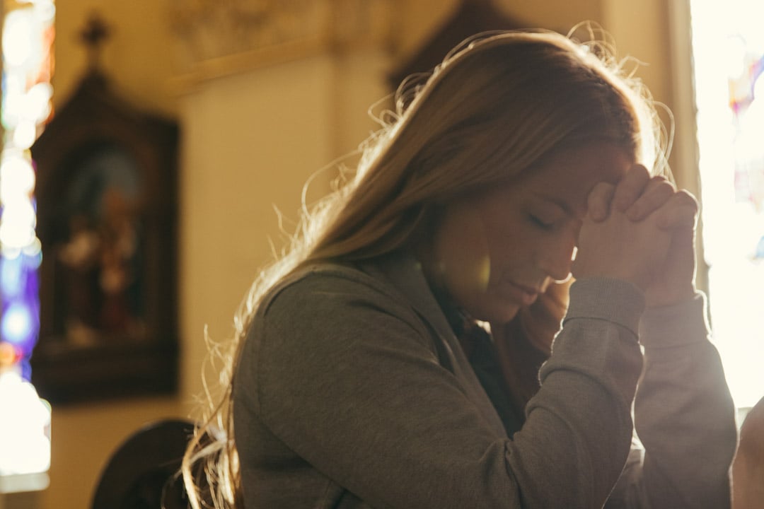 A woman kneels praying alone in a church