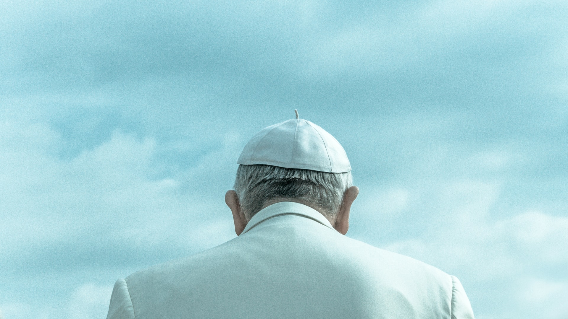A photo of the back of Pope Francis' head as he looks out a blue sky