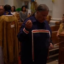 An elder performs a smudge ceremony with a priest behind him