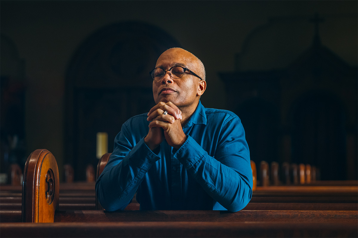 Man kneels in a church smiling as he prays