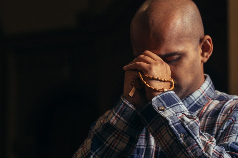 Man kneels in church while praying the rosary