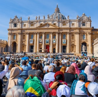 A crowd of people from around the world sit outside of St. Peter's Basilica in the Vatican