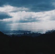 Clouds with light streaming through them, shining down onto a dark cityscape