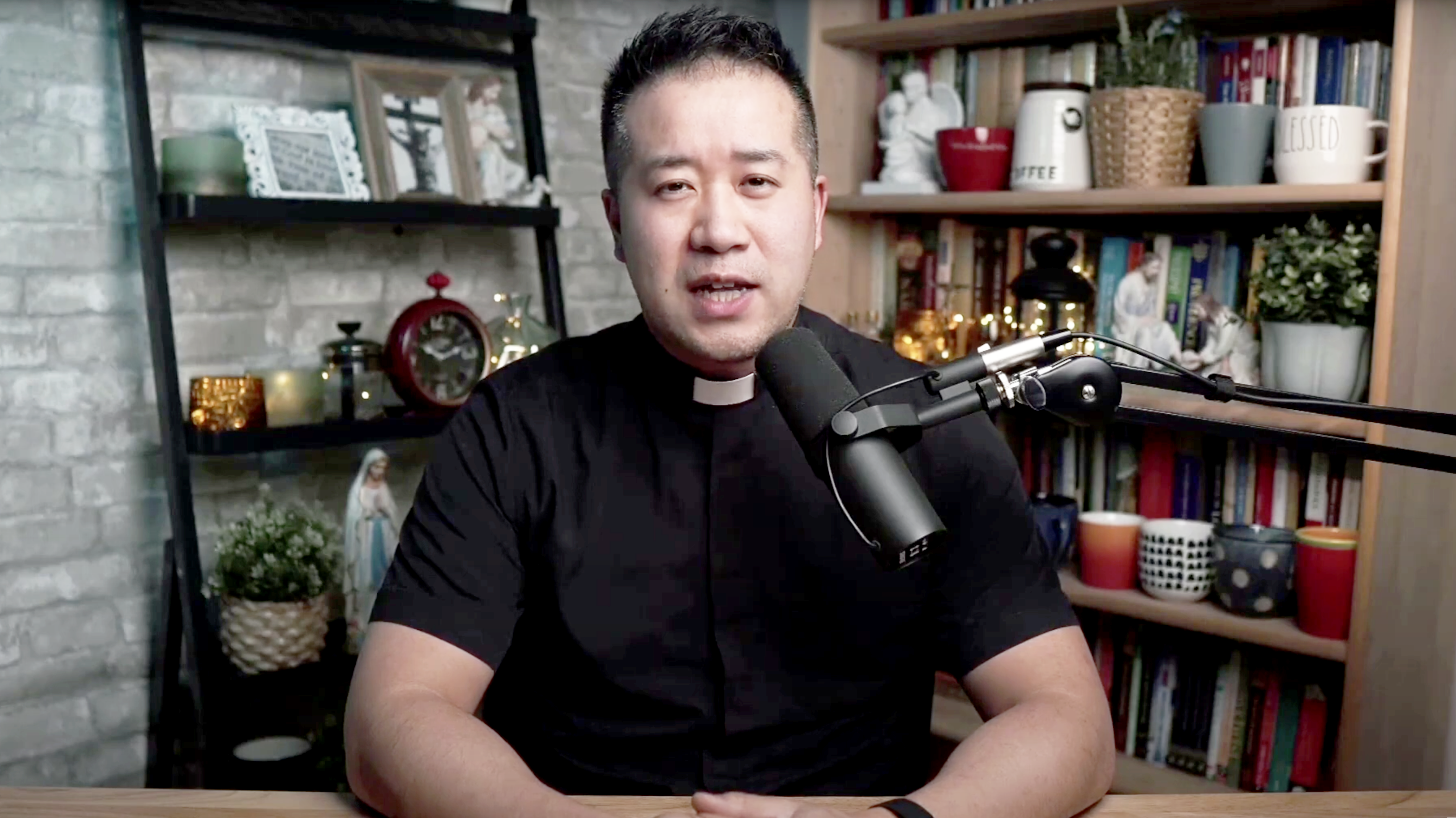 Fr Eric Mah sitting at his desk with a microphone