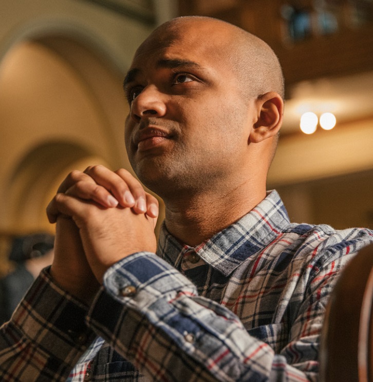 A man kneels in prayer in a church