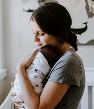 A mother holds her newborn child in her arms. In a nursery, the baby is in a swaddle