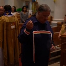 An elder performs a smudge ceremony with a priest behind him