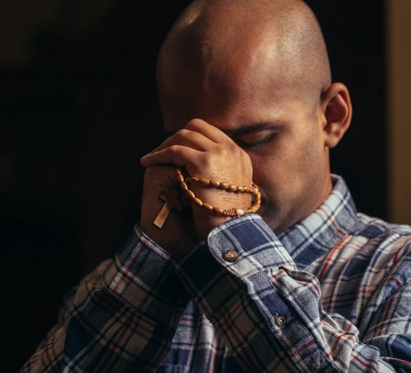 A man kneels in a church while praying the rosary