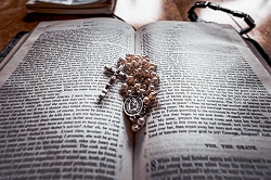 A Bible opened on a table with a rosary laying on top of it