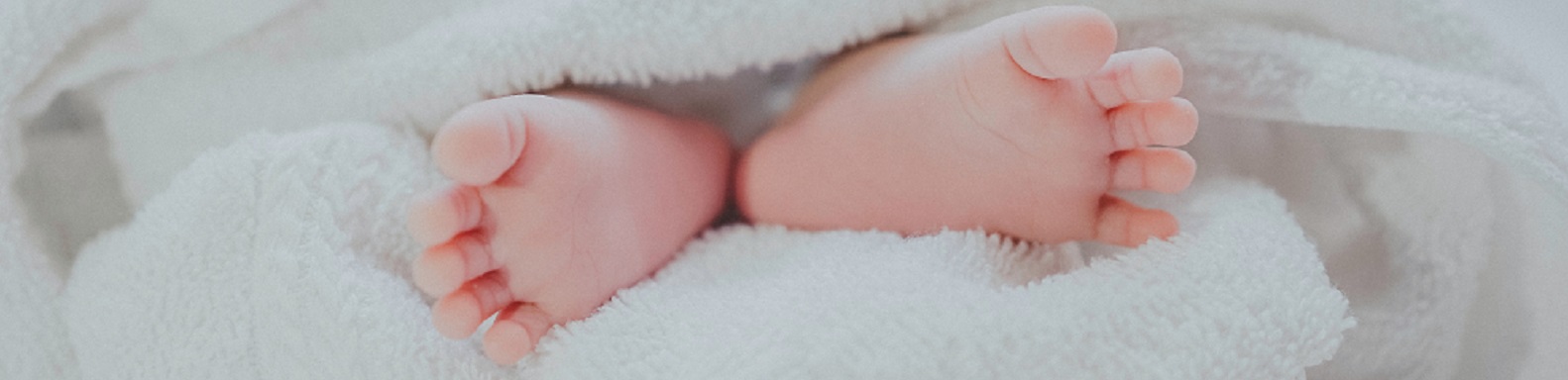 A newborn's feet stick out from soft white blankets