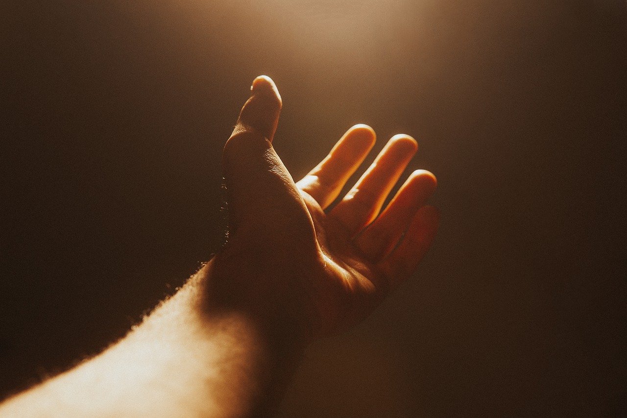 A hand reaches out in the darkness towards a single source of light