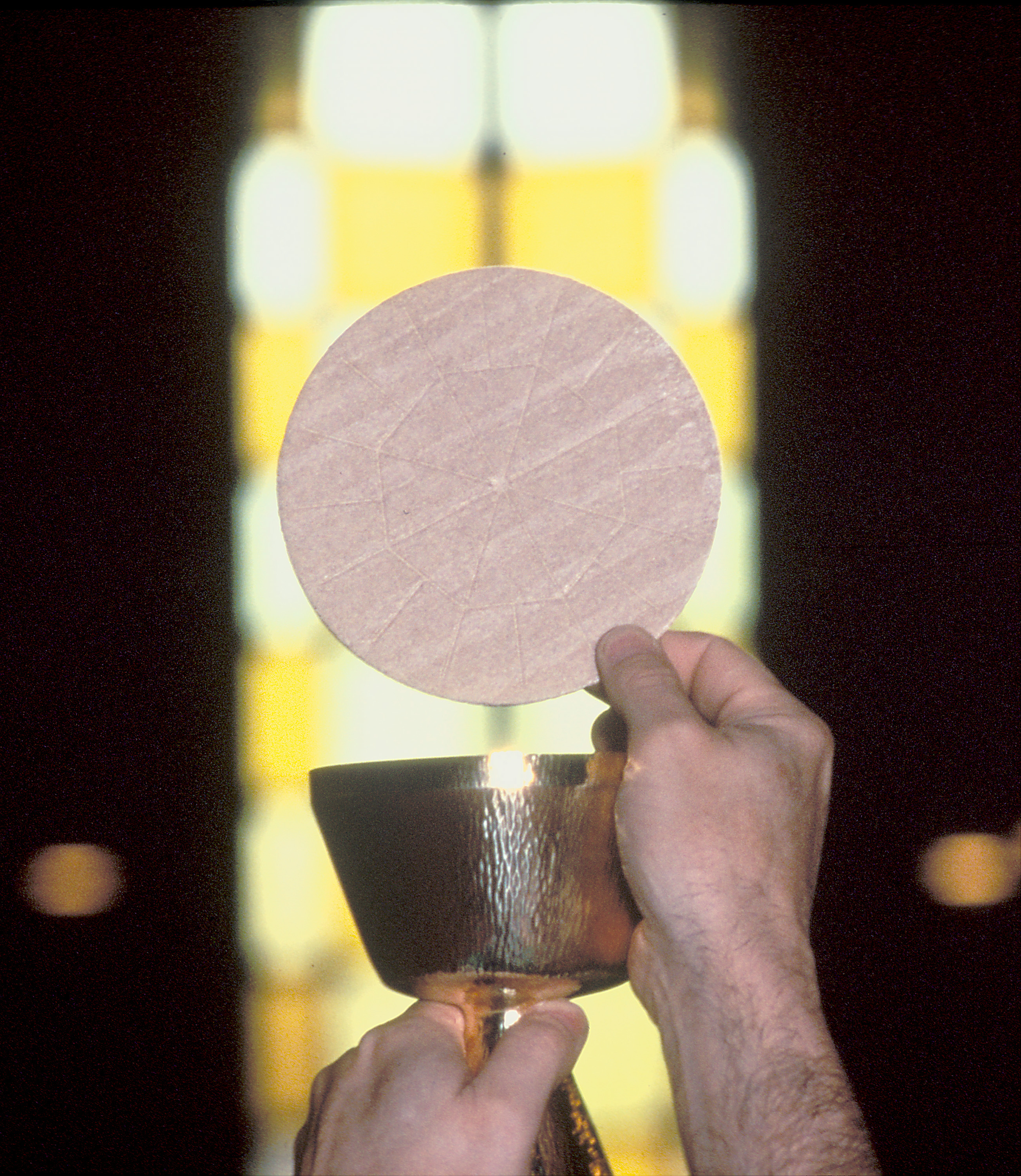 The Eucharist being held up by a priest in front of a stained glass window