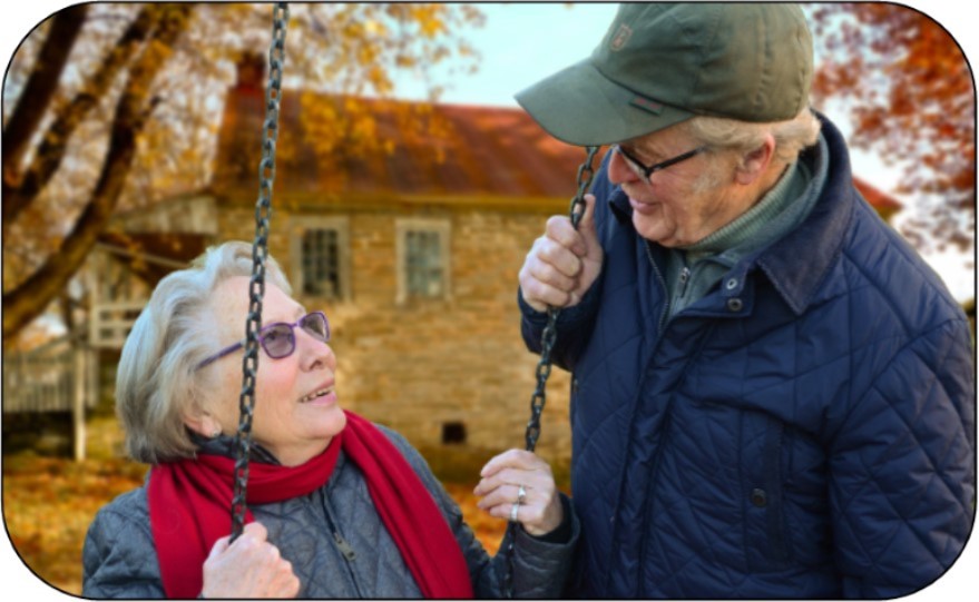 elderly couple, woman is on a swing, husband next to her and they are smiling at each other