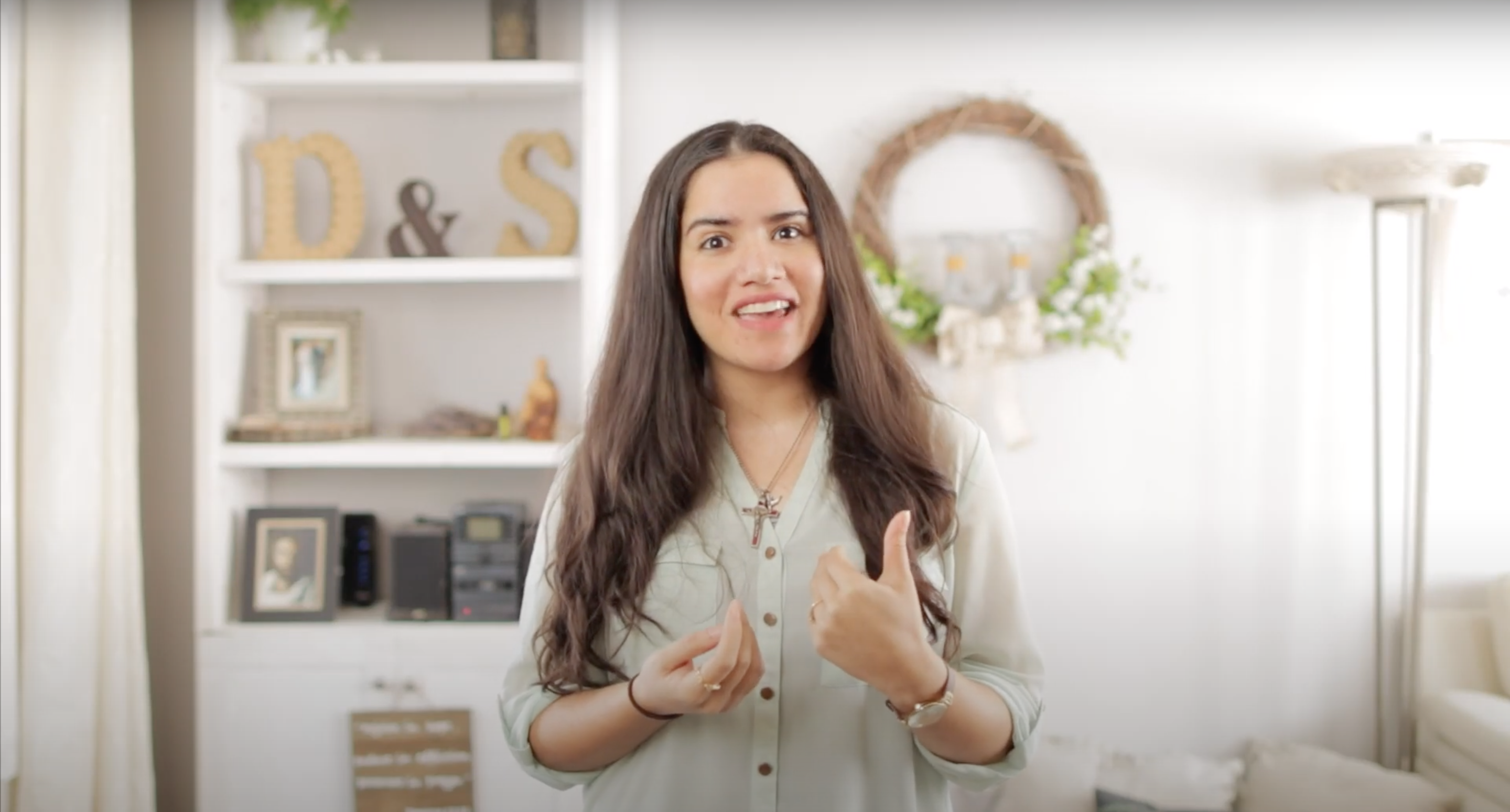 Image of young woman inside a home speaking to the camera with her hands in motion to describe what she's saying