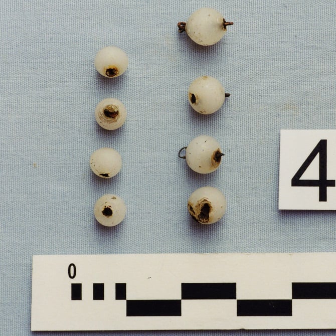 White spherical buttons with rusty metal wire for attaching to clothing.