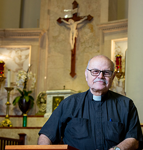 A retired priest smiles as he stands in the sanctuary of a church